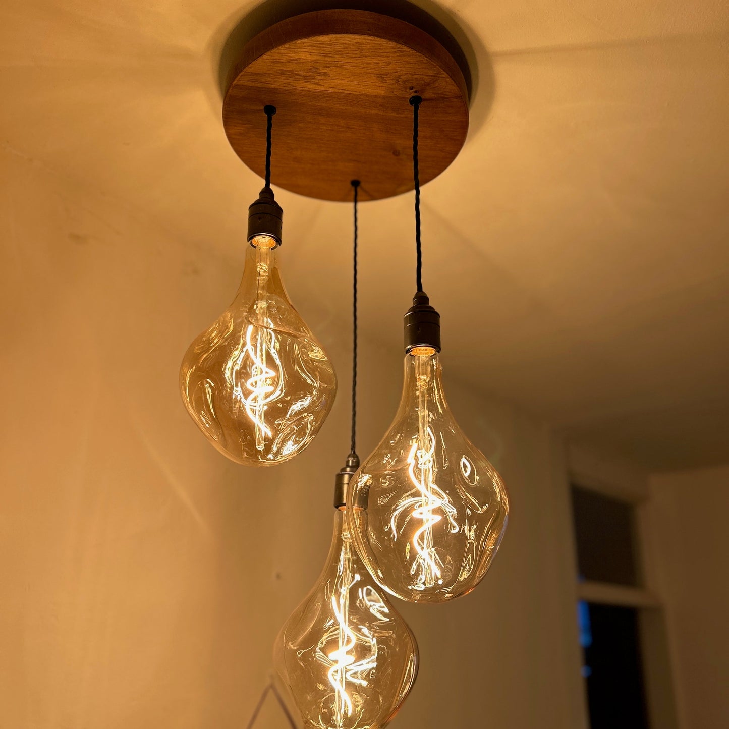 Three vintage-style light bulbs hanging from a wooden ceiling fixture.